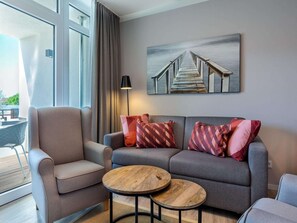 Ein modernes Wohnzimmer mit einer Couch, einem Sessel und zwei runden Holztischen.