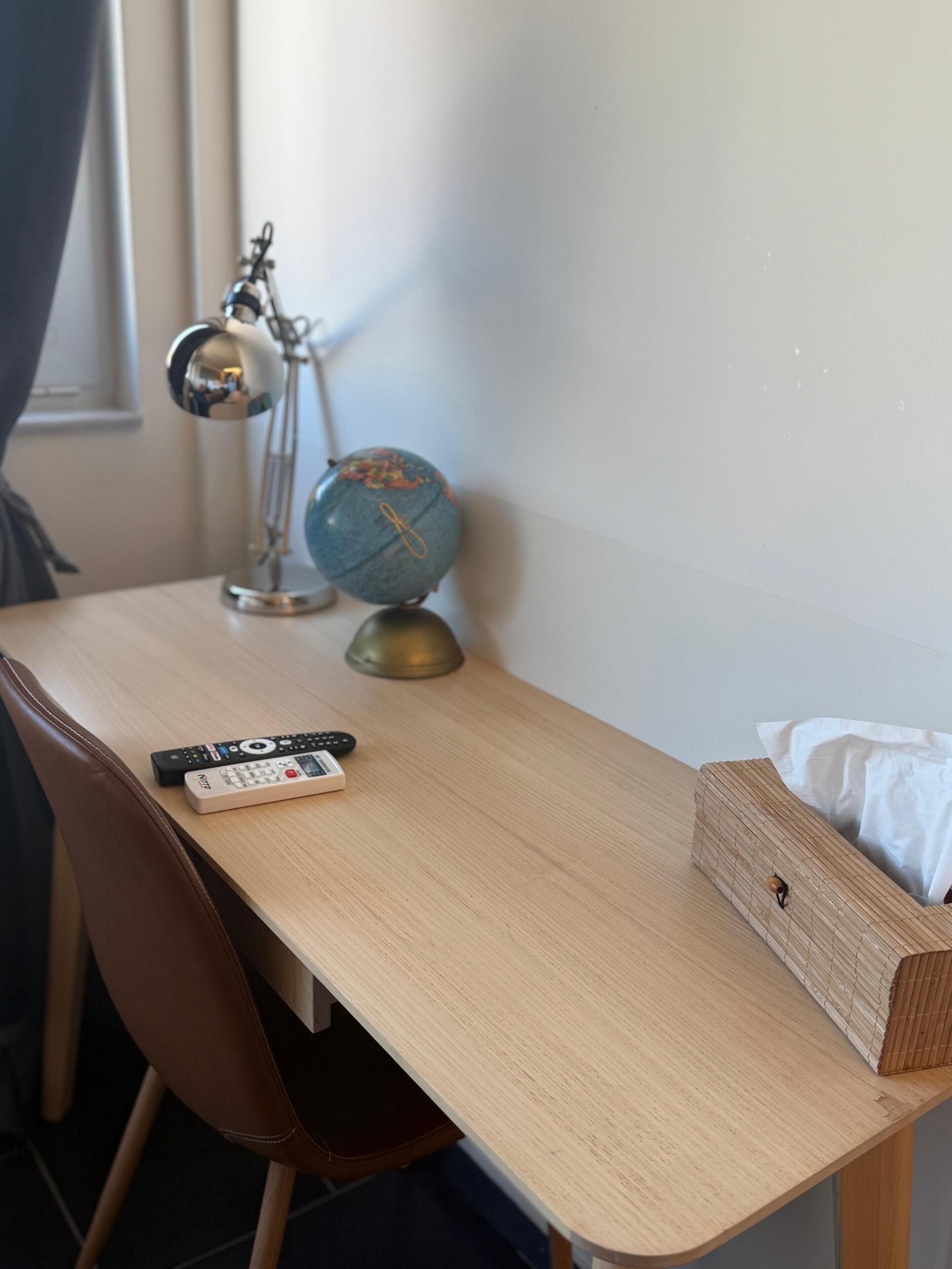Una scrivania di legno con un mappamondo, una lampada e un telecomando.