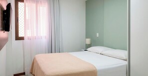 A single bed with a white mattress and a beige blanket, a bedside table with a lamp, and a window with sheer curtains. - Apartment With Balcony 350m From the Beach by MME (Maceió)