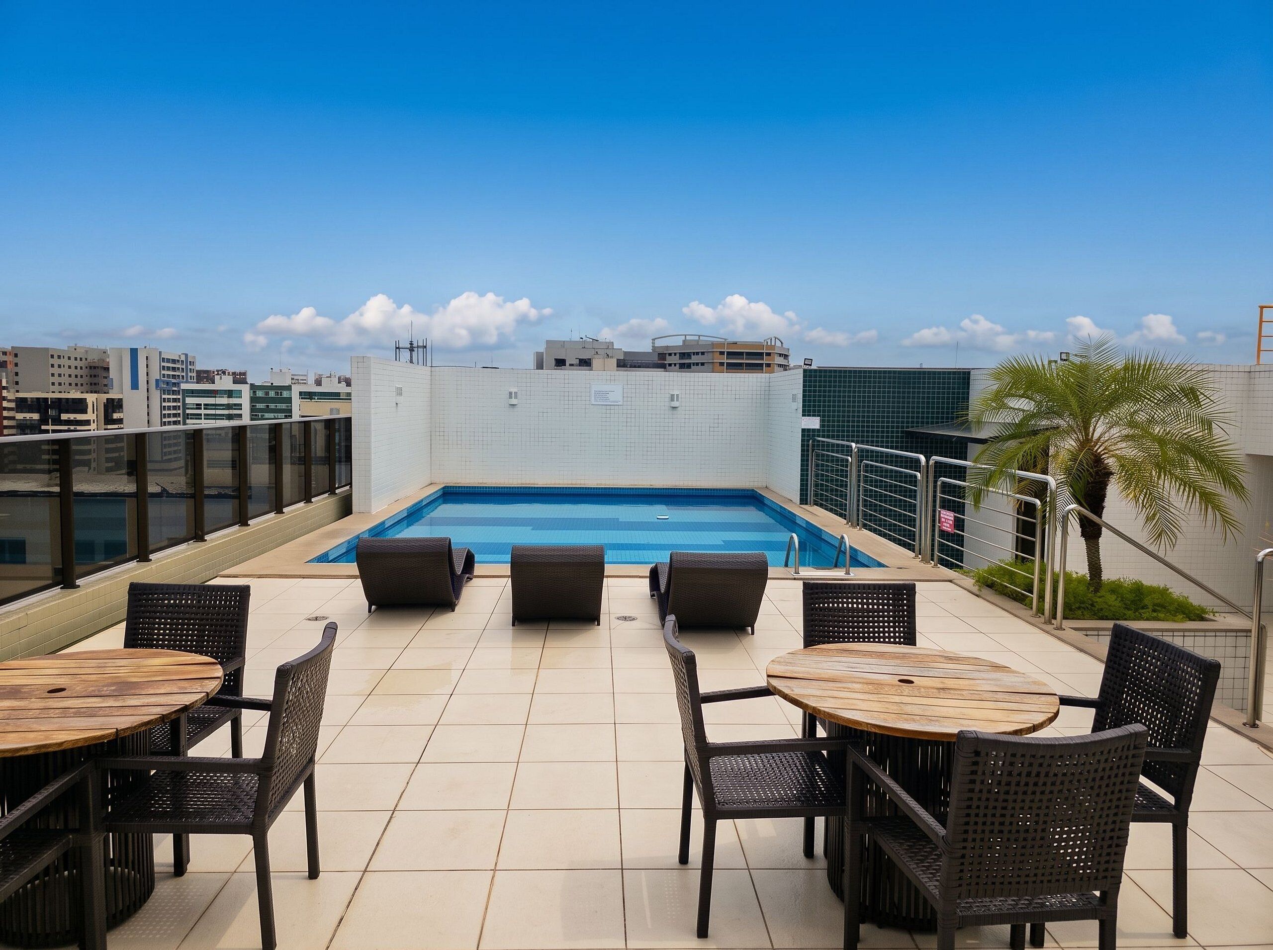 Zona de piscina en la azotea con vista despejada del horizonte de la ciudad, rodeada de pisos de baldosas y amueblada con sillas y mesas de mimbre.