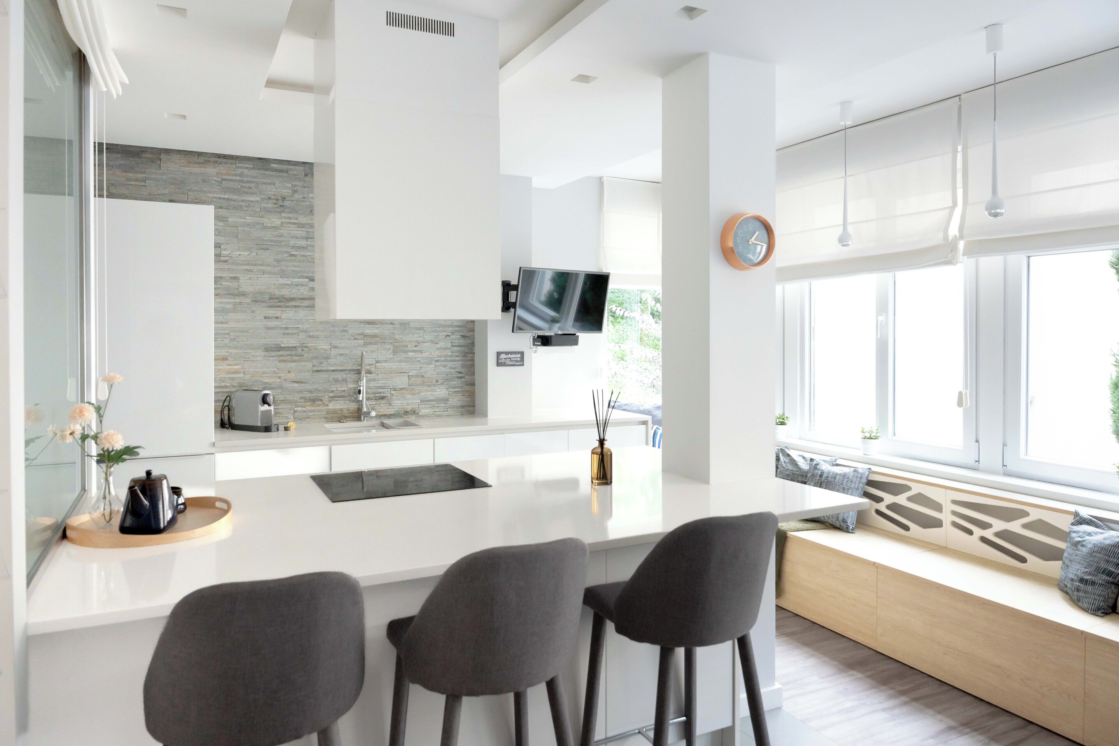 A modern kitchen with a central island, bar stools, a built-in TV, and a window seat with cushions.