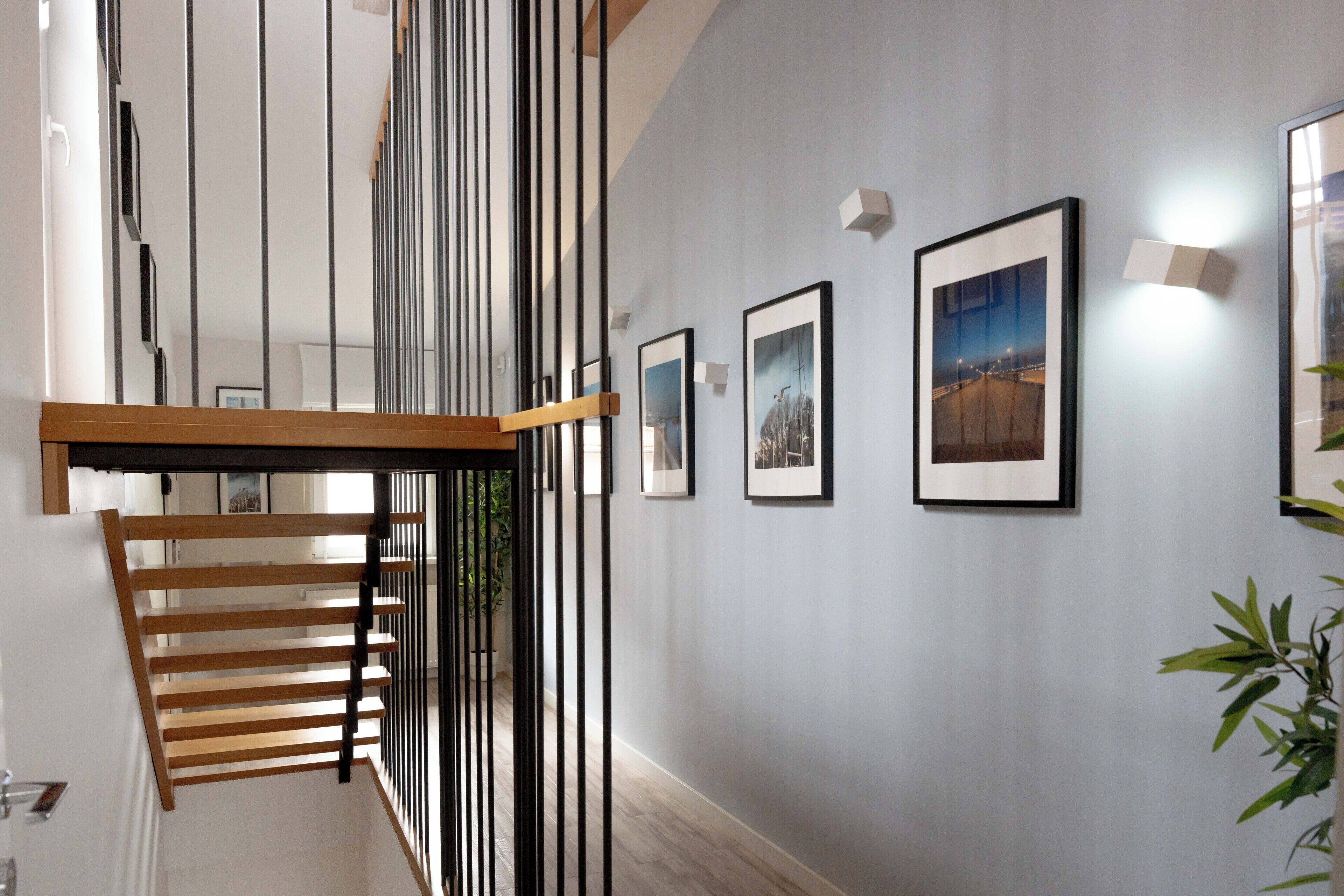 A staircase with a wooden handrail and black vertical supports, leading to a landing with framed pictures on the wall.