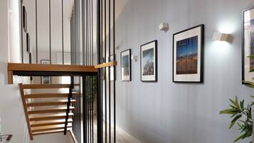 A staircase with a wooden handrail and black vertical supports, leading to a landing with framed pictures on the wall.