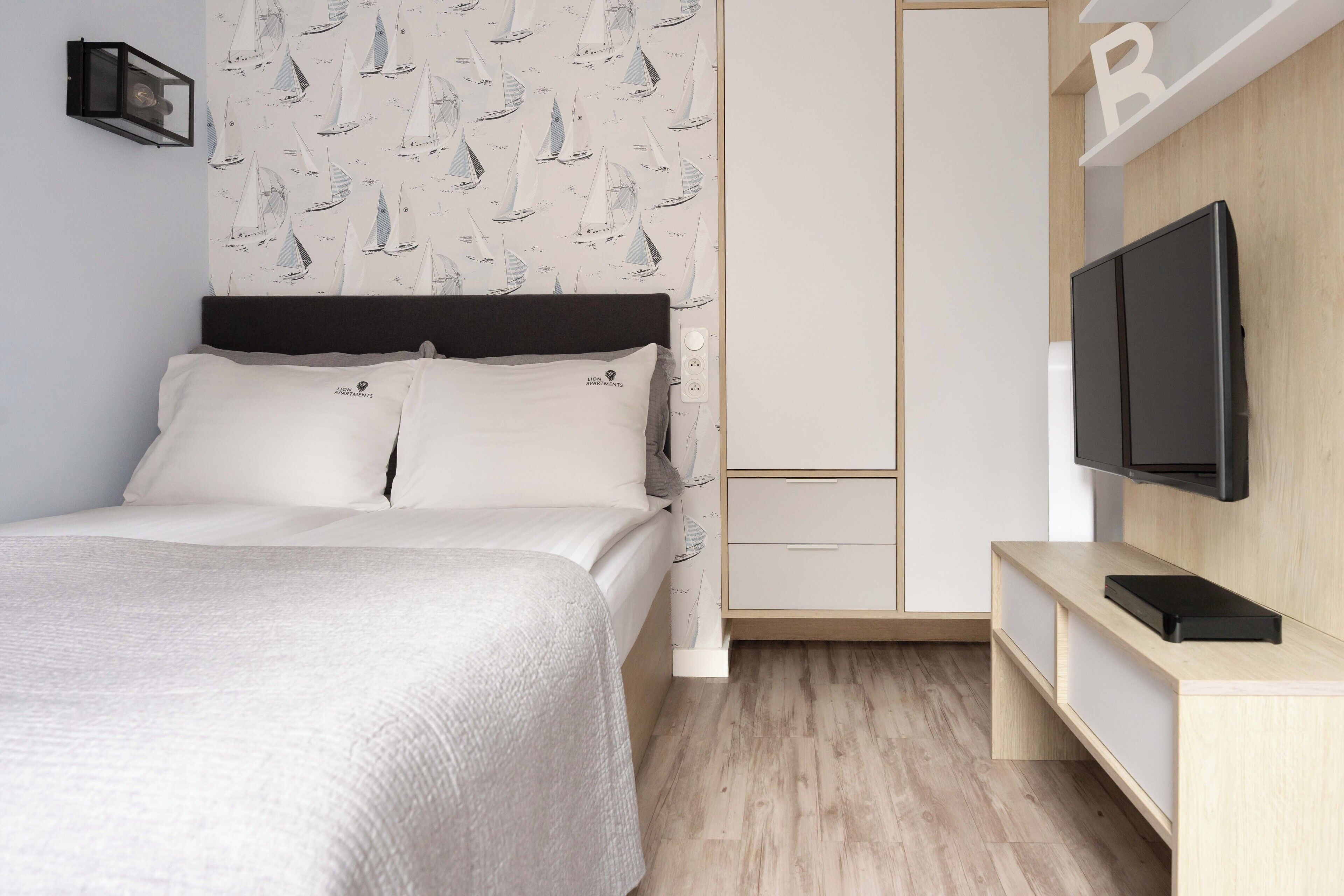 Un dormitorio con cama, televisor, armario y pared con estampado de velero.