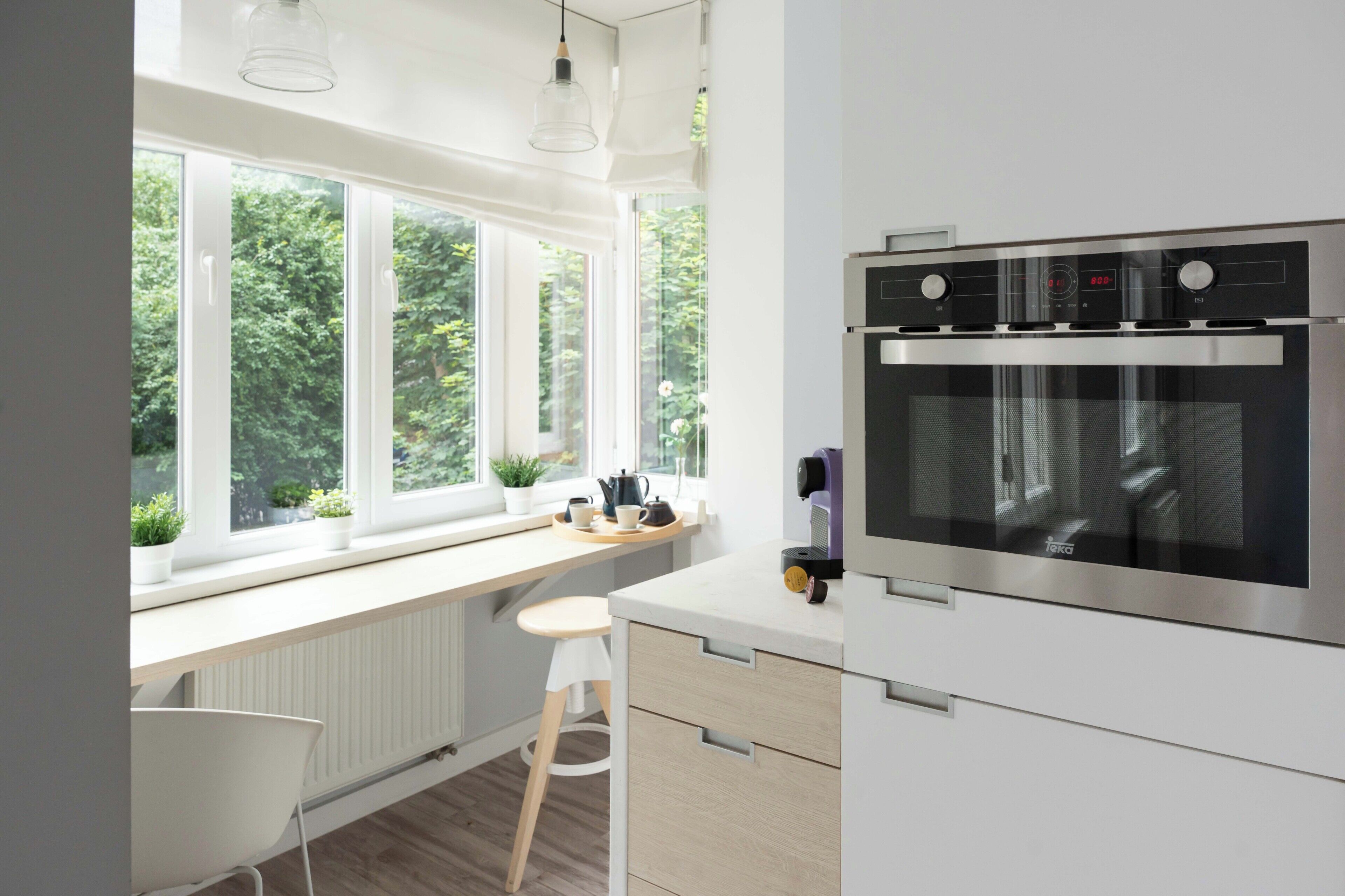 Et moderne køkken med indbygget ovn, et vindue med udsigt til grønne områder, og en hvid stol.