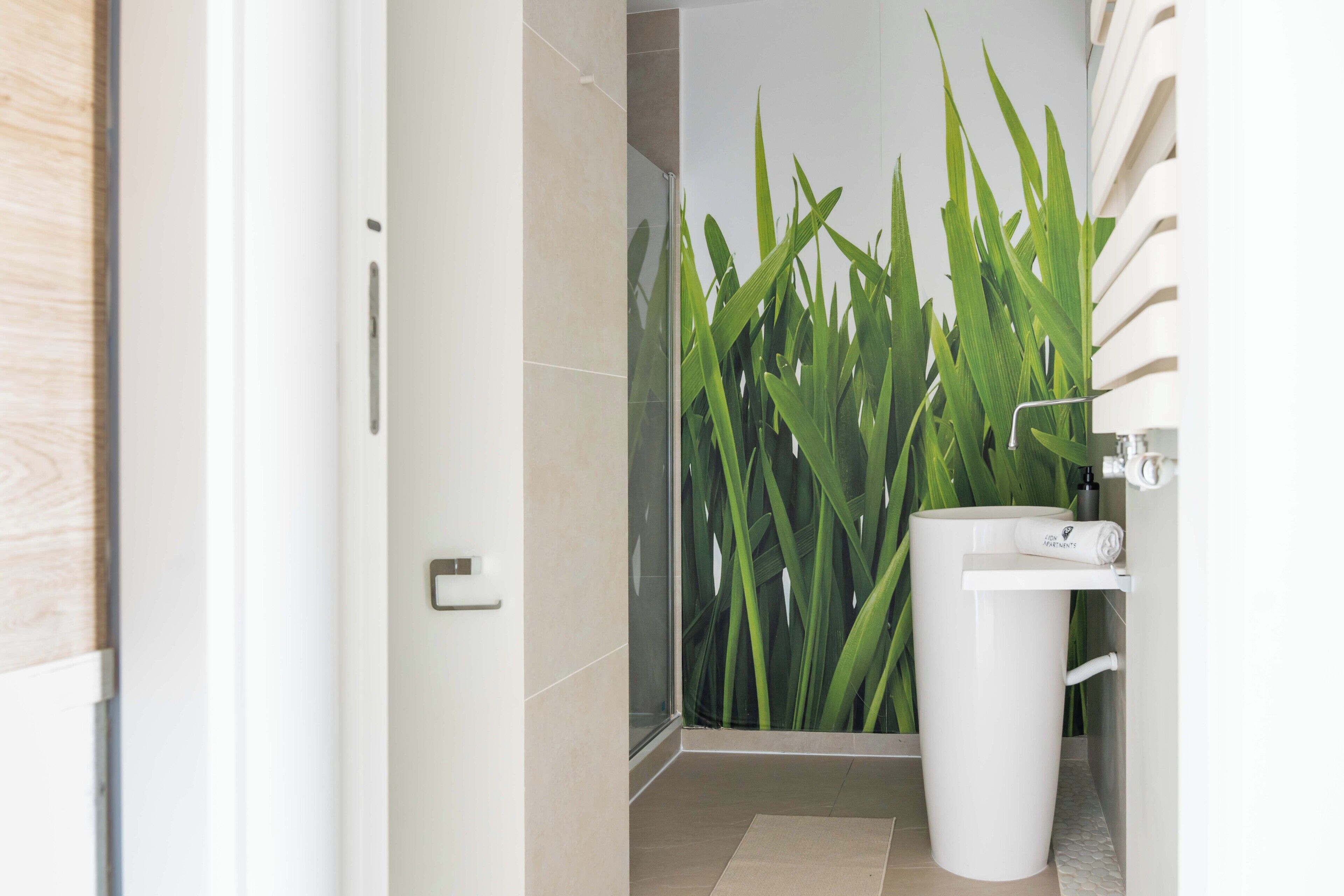 Un baño con ducha, lavamanos y una planta verde grande.
