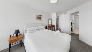 Quarto de hotel com uma cama grande, uma mesa de cabeceira com abajur, um espelho e um quadro na parede.
