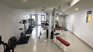 Uma academia com equipamentos de cardio, aparelhos de musculação e um banco.