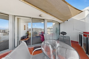 A balcony with a glass door, a chair, a table, and a barbecue grill. - Top Floor Braddon | Sunset Views to Black Mountain (Braddon)