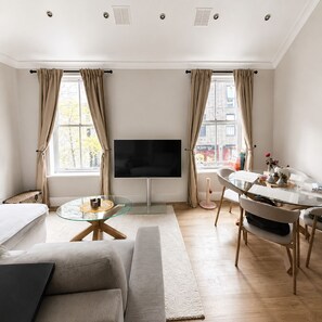 Ein modernes Wohnzimmer mit Flachbildfernseher, einem Glastisch, einer Couch und einem Essbereich mit Tisch und Stühlen.