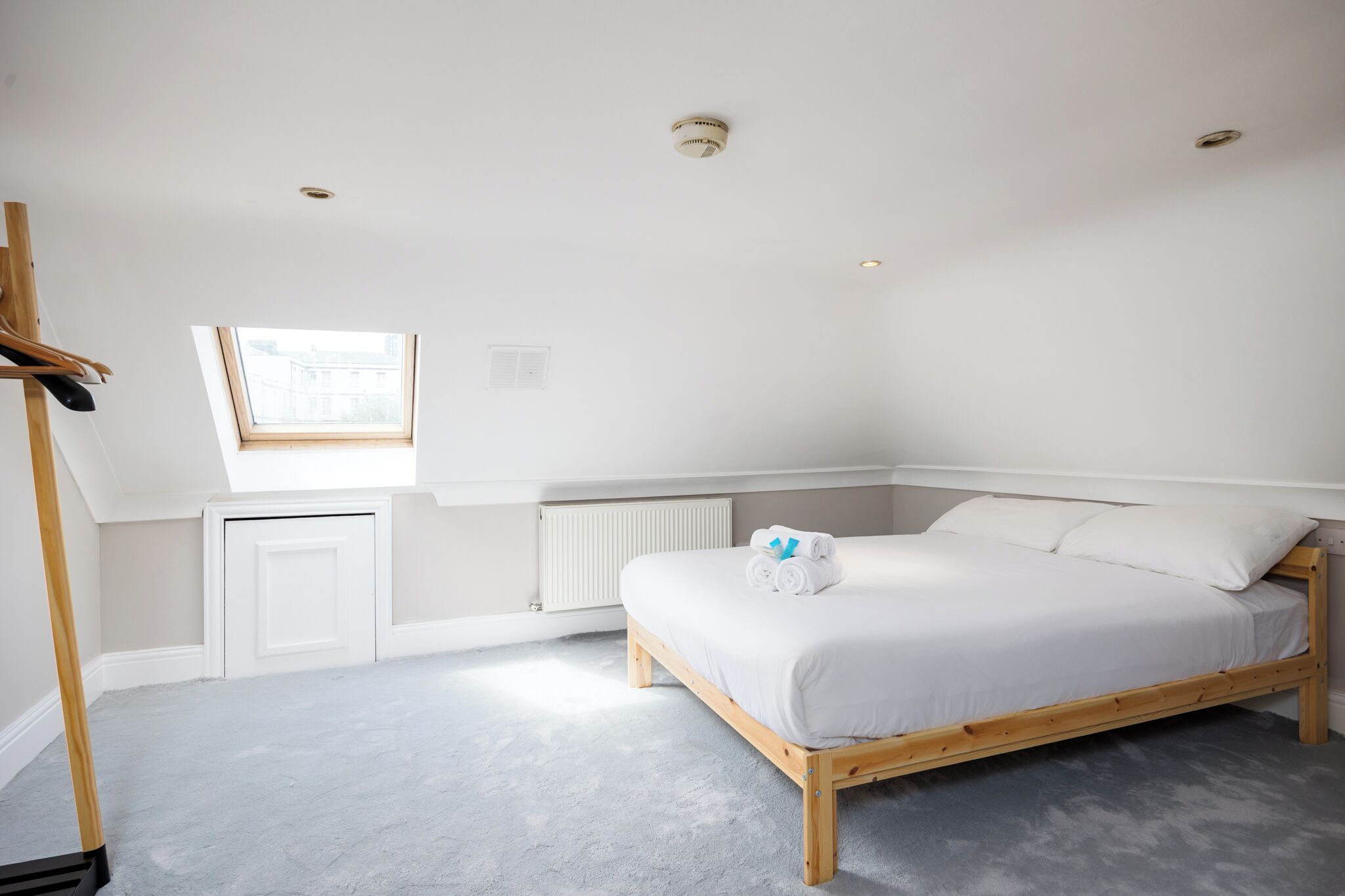 A bedroom with a bed, a window, a radiator, and a wooden wardrobe.