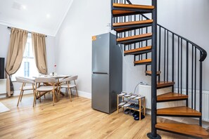 Une cuisine moderne dotée d’un réfrigérateur encastré, un coin repas avec une table et des chaises, et un escalier en bois.