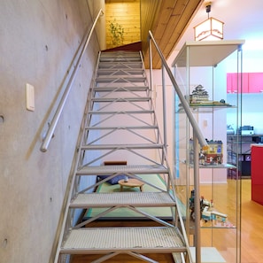 A metal staircase with a handrail, leading to a room with a bed and a small table.