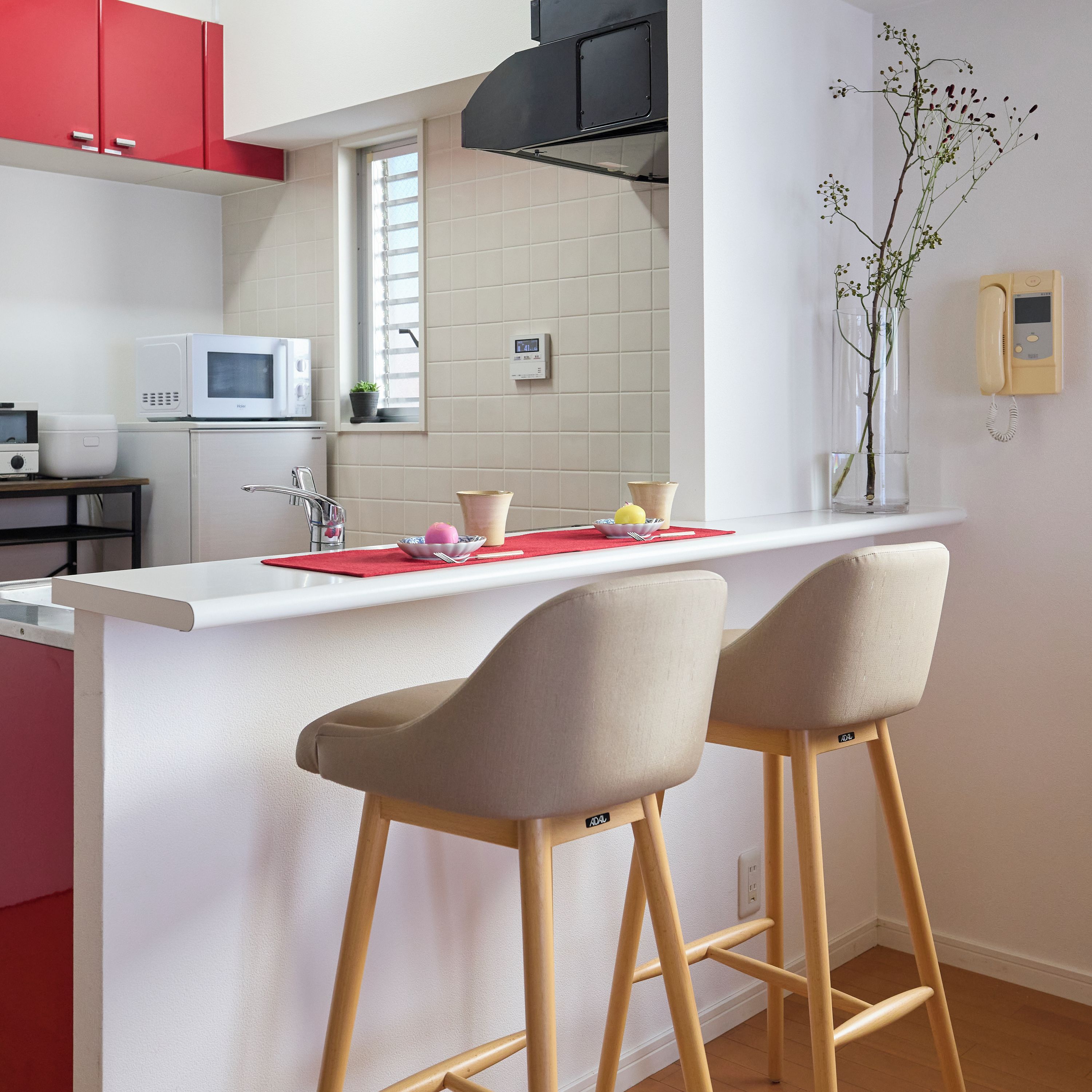 A modern kitchen with a white countertop, red cabinets, and two bar stools.