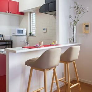 A modern kitchen with a white countertop, red cabinets, and two bar stools.