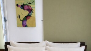 Uma cama com roupa de cama branca e um quadro abstrato colorido na parede.