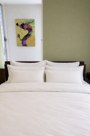 A bed with white bedding and a colorful abstract painting on the wall.