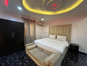 Ein Schlafzimmer mit Bett, Kopfteil, Kleiderschrank und einer Decke mit runder Beleuchtung.