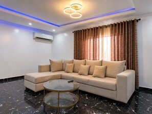 Ein modernes Wohnzimmer mit einem Ecksofa, einem Glastisch und einer Deckenleuchte.