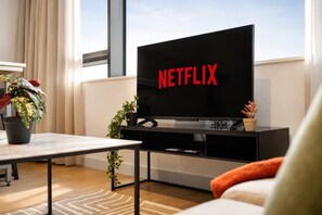 A modern living room with a flat-screen TV displaying the Netflix logo, a coffee table, a sofa, and potted plants. - Modern Studio by Stay With Us (Salford)