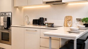Una cocina moderna con electrodomésticos de acero inoxidable, una encimera blanca y una tabla de cortar de madera.