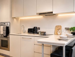 A modern kitchen with stainless steel appliances, a white countertop, and a wooden cutting board. - Modern Studio by Stay With Us (Salford)