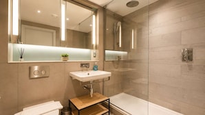 Un baño moderno con ducha envuelta en vidrio, un lavamanos blanco y un inodoro.