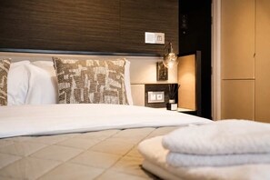A neatly made bed with white linens, a headboard with a patterned design, and a bedside lamp. - Modern Studio by Stay With Us (Salford)