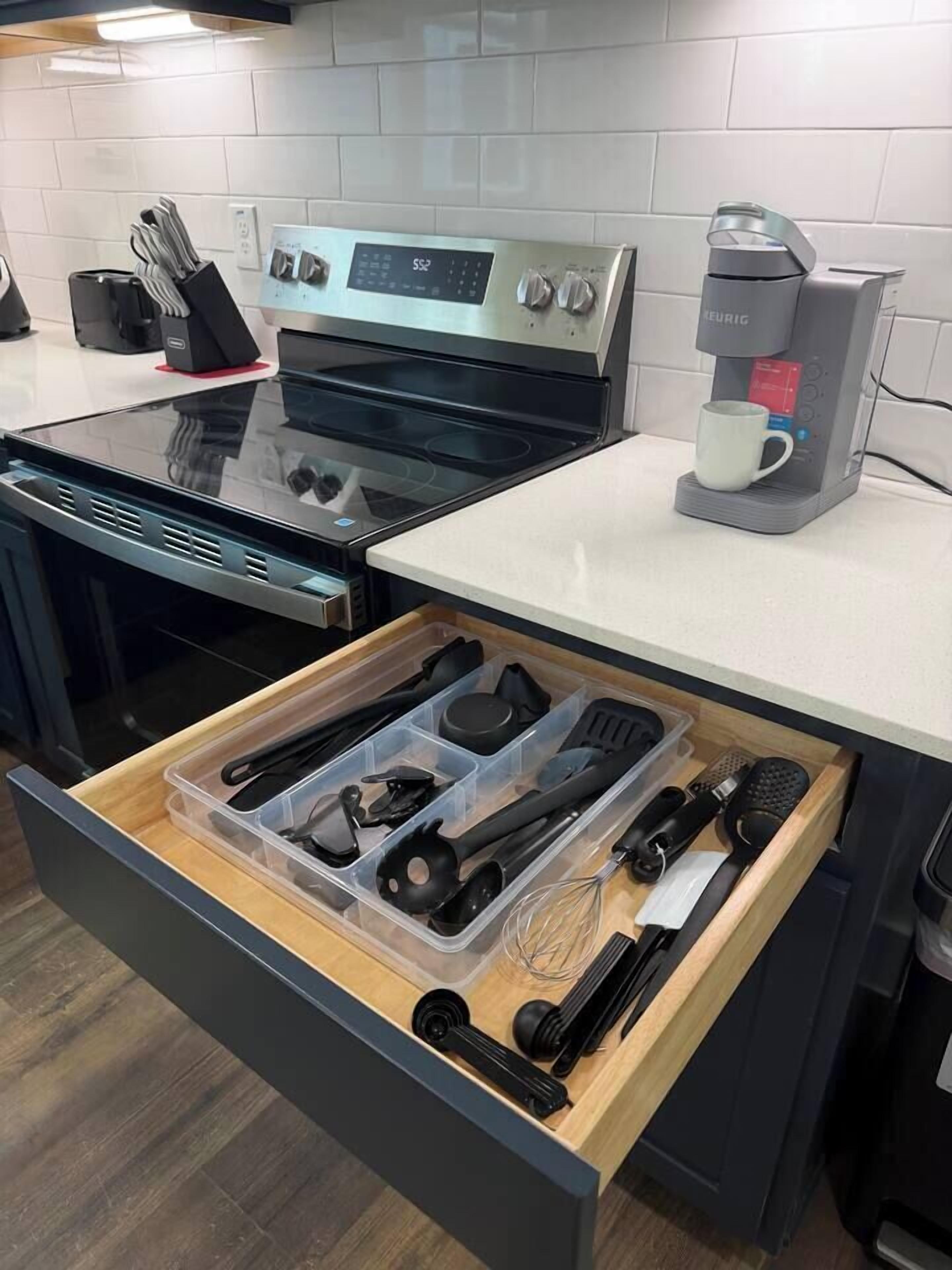 Una cocina con estufa de acero inoxidable, una cafetera Keurig y un organizador de cajones para utensilios.