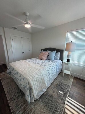A bedroom with a bed, a ceiling fan, a nightstand, and a window with blinds.