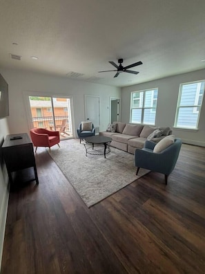 A spacious living room with a dark wood floor, a ceiling fan, a sofa, a coffee table, and a red armchair.