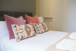 Una cama bien hecha con almohadas estampadas y una toalla doblada al lado.