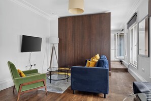 Una sala de estar moderna con un televisor de pantalla plana, un sillón verde, un sofá azul y una pared de acento de madera.