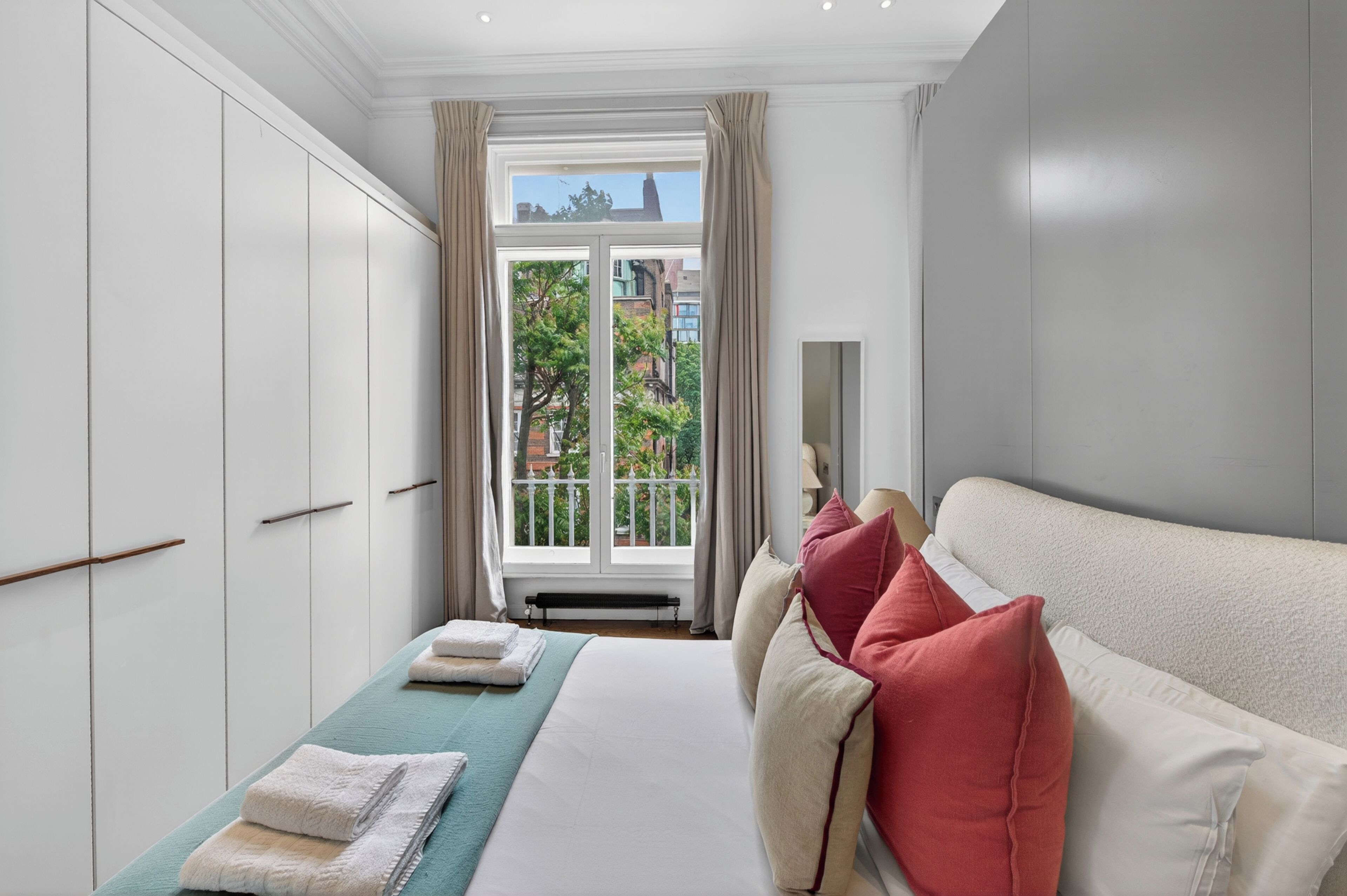 A hotel room with a bed, a window with curtains, a radiator, and a view of buildings outside.