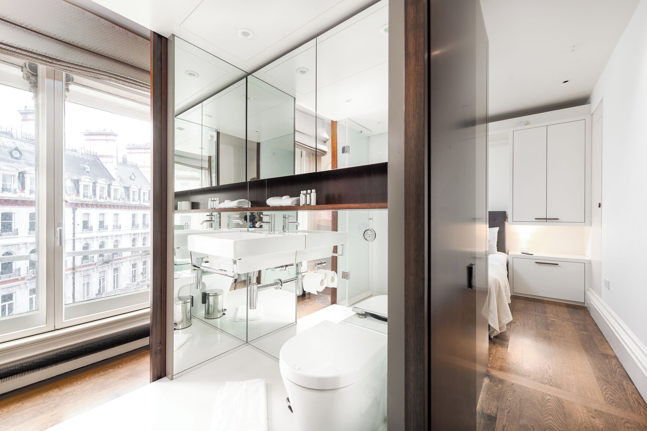 A modern bathroom with a large window, a toilet, a sink, and a mirror.