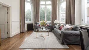 Ein modernes Wohnzimmer mit einem grauen Sofa, einem runden Couchtisch und Blick auf eine Stadtlandschaft durch große Fenster.