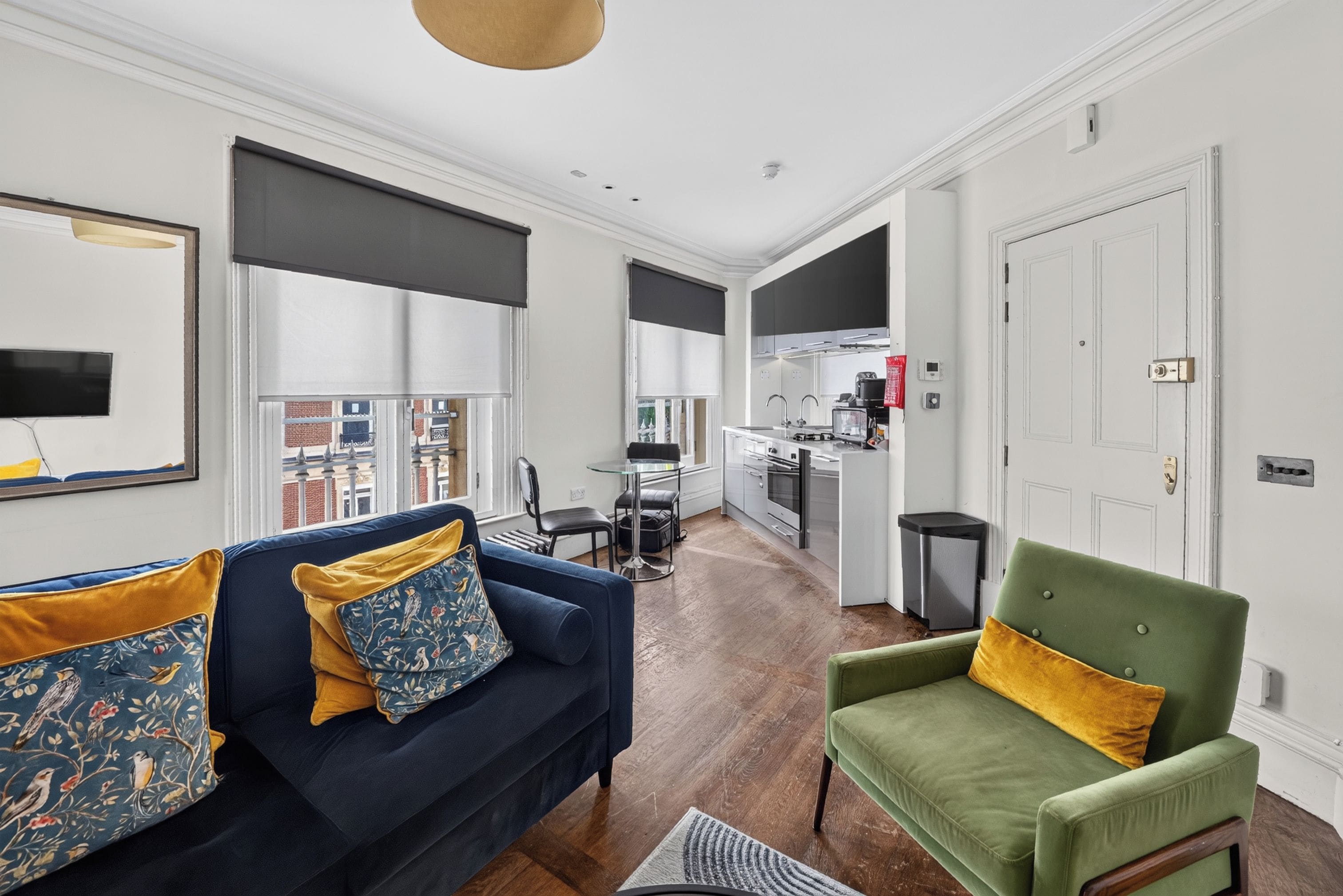 A modern living room with a sofa, armchair, and a dining area with a kitchen in the background.