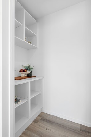 A white interior with a wooden floor, a white wall, and a white shelving unit with a bowl of fruit and a book. - The Meadow - 5 Bedroom HOME - Relax and Enjoy (Christchurch)