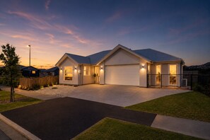 A residential house with a garage, driveway, and a well-lit entrance. - The Meadow - 5 Bedroom HOME - Relax and Enjoy (Christchurch)