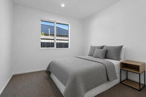 A bedroom with a single bed, a nightstand, and a window with a view of a house and trees. - The Meadow - 5 Bedroom HOME - Relax and Enjoy (Christchurch)