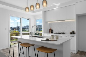 Une cuisine moderne dotée d’un îlot central, de tabourets de bar, d’un four encastré et de luminaires suspendus.