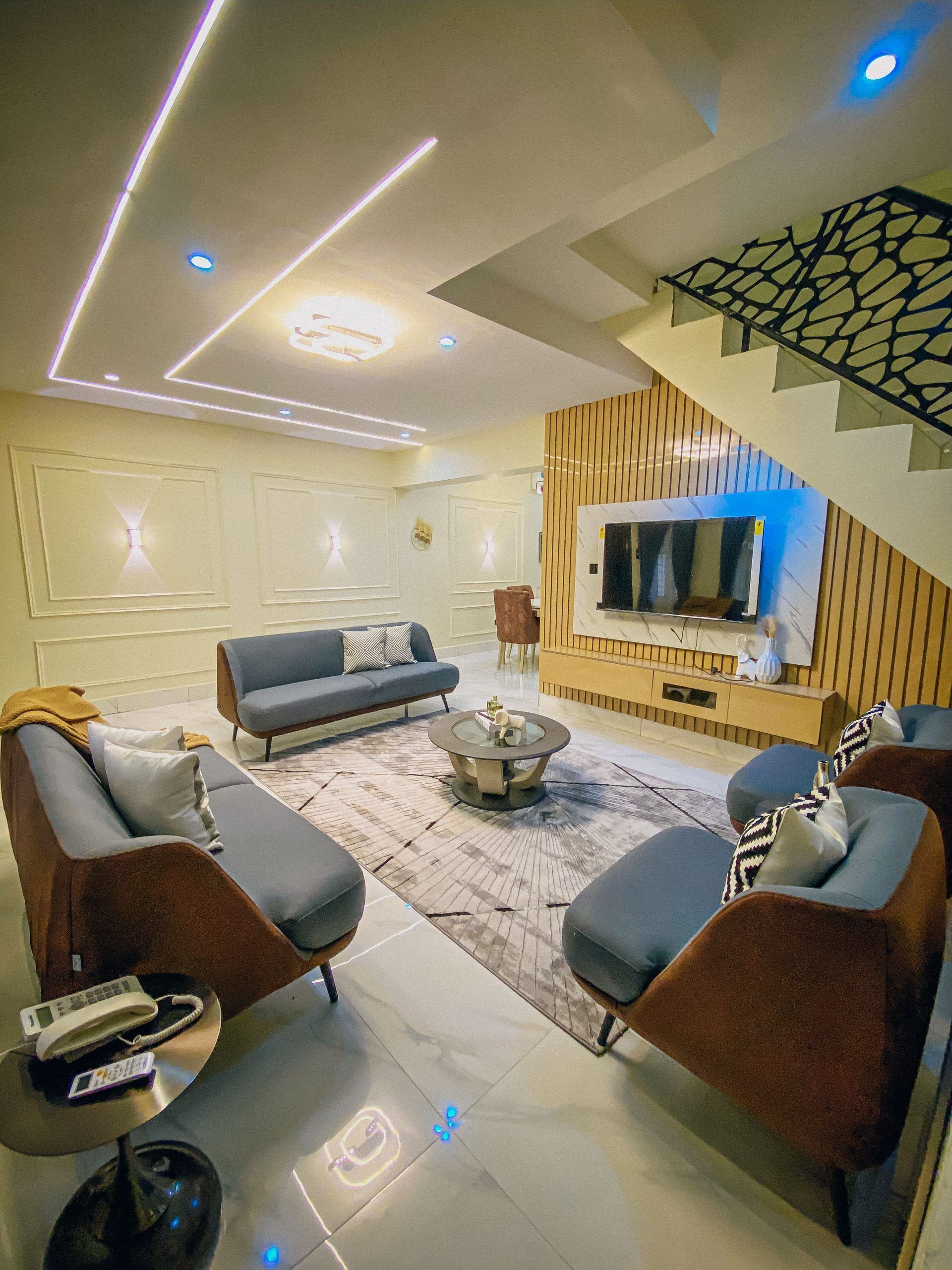 A modern living room with a sofa set, a coffee table, and a flat-screen TV mounted on a wooden panel wall.