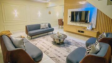 A modern living room with a sofa set, a coffee table, and a flat-screen TV mounted on a wooden panel wall.