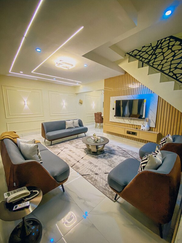 A modern living room with a sofa set, a coffee table, and a flat-screen TV mounted on a wooden panel wall.