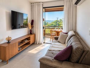 A modern living room with a flat-screen TV, wooden console, sofa with cushions, and a balcony with a table and chairs.