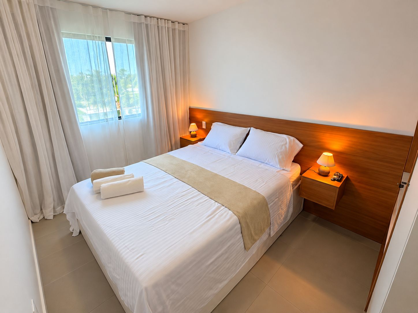 A hotel room with a large bed, two bedside tables with lamps, and a window with curtains.