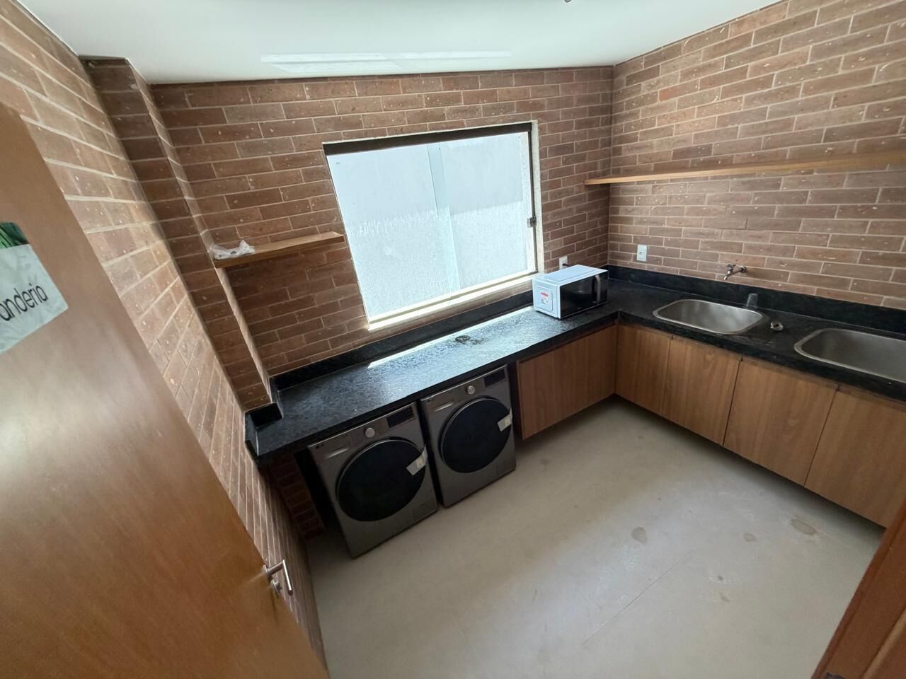 A compact kitchen with a brick backsplash, a window, two washing machines, and a sink.