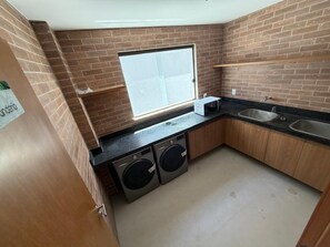 A compact kitchen with a brick backsplash, a window, two washing machines, and a sink.