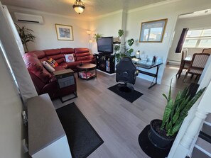 A living room with a red leather sofa, a black office chair, a television, and a dining area with wooden chairs.