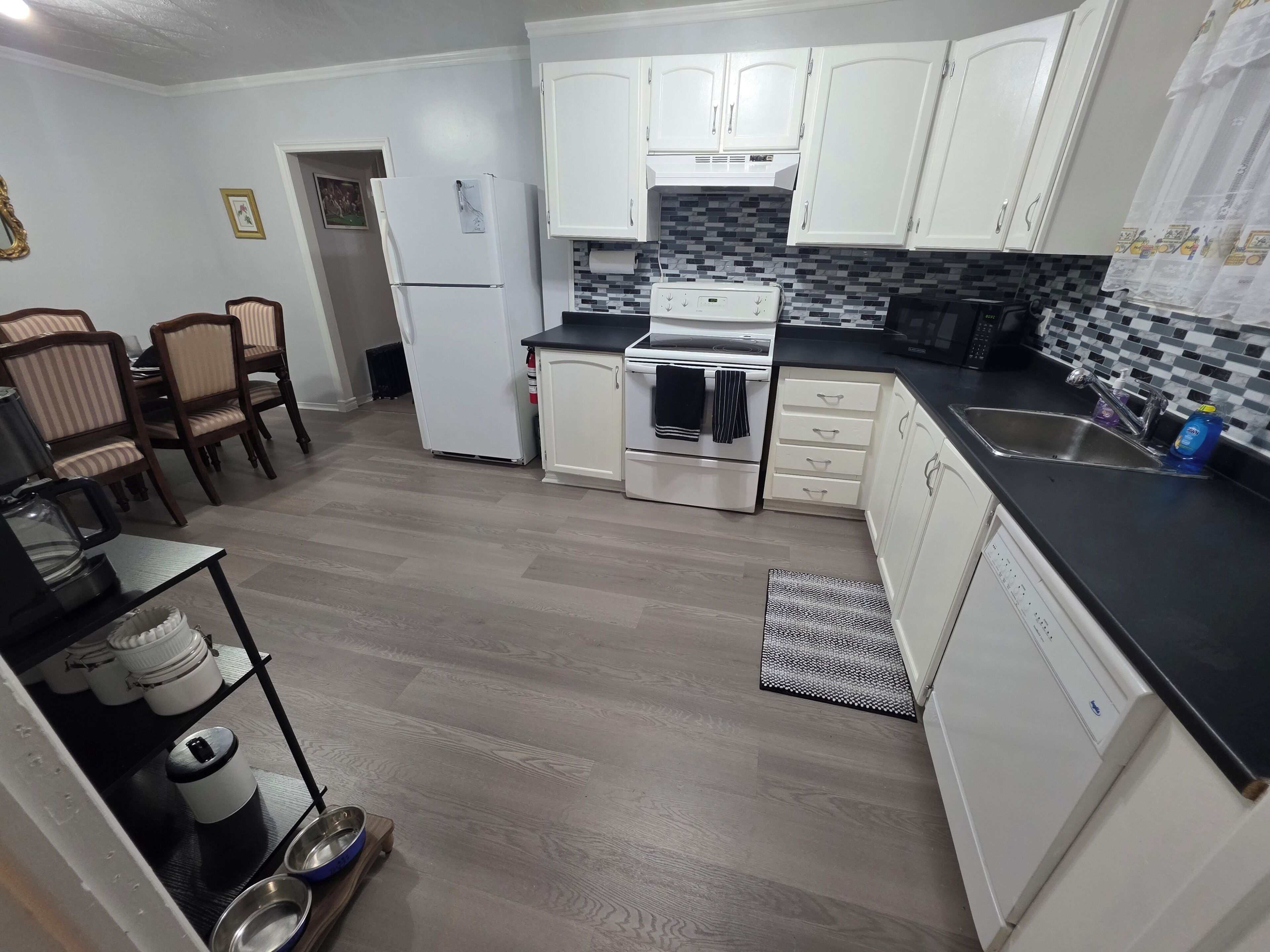 A compact kitchen with white cabinets, a black countertop, and a tiled backsplash.